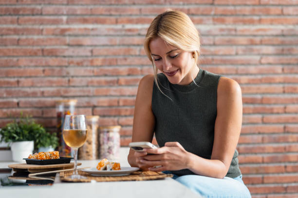 istock Pretty young woman eating sushi while using smartphone in the kitchen at home 2190067953