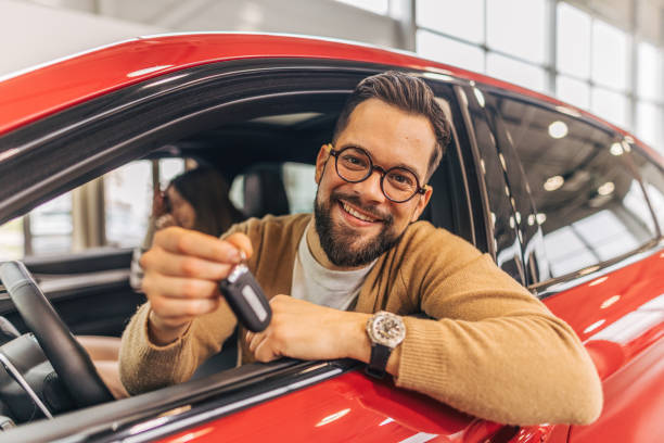 istock Man holding keys and sitting inside new car in showroom 2190086868