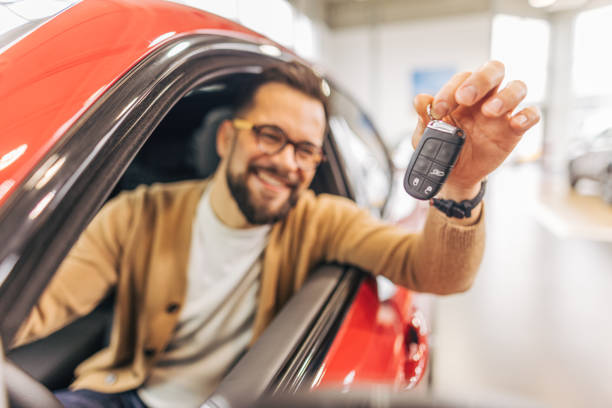 istock Man holding keys and sitting inside new car in showroom 2190087237