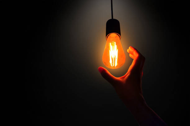 istock Creative idea concept. Hand reaching to a glowing light bulb on black background. 2190091456