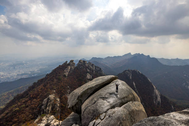seoul, south korea - october 23, 2023: people hiking and climbing to baegundae mountain and resting at the peak in bukhansan national park in seoul.