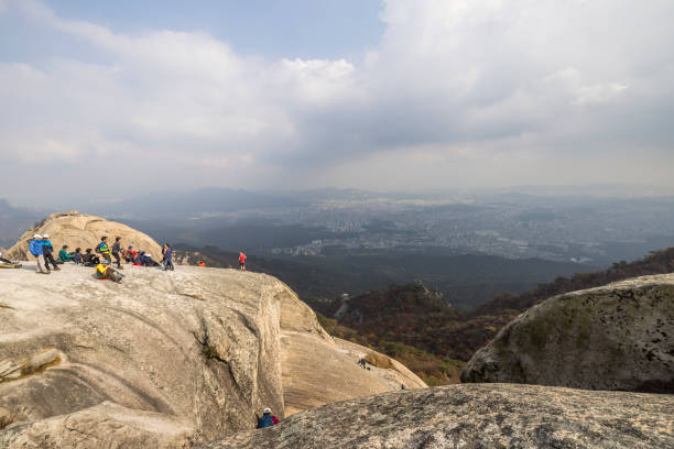 seoul, south korea - october 23, 2023: people hiking and climbing to baegundae mountain and resting at the peak in bukhansan national park in seoul.