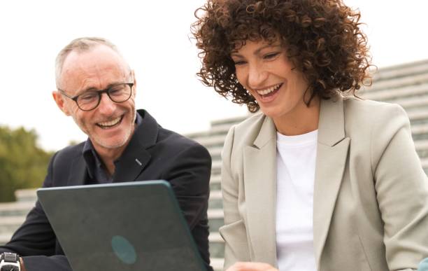 istock Cheerful business colleagues using netbook sitting on steps 2190094704