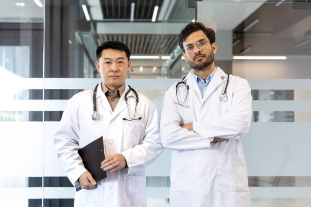 istock Confident doctors standing in modern hospital hallway wearing white coats and stethoscopes, demonstrating professionalism and teamwork in a healthcare environment. 2190096702
