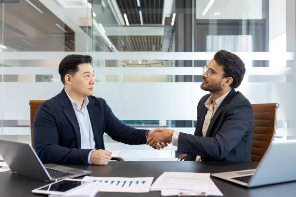 istock Confident handshake between two businessmen in modern office setting, symbolizing partnership, trust, and successful deal with laptops and documents on table 2190098058