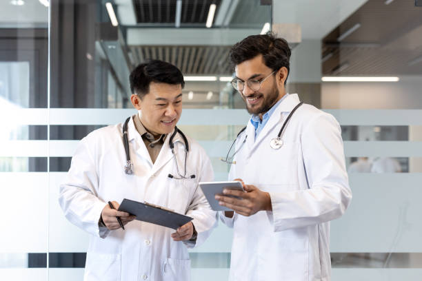 istock Two doctors in white coats engaged in professional discussion, using digital tablet in modern hospital setting. Collaboration illustrates teamwork and technology in healthcare environment. 2190098238