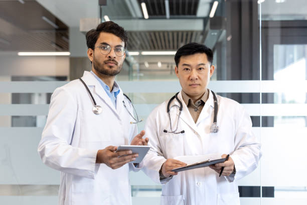 istock Two confident doctors in white lab coats with stethoscopes holding tablet and clipboard in modern medical office 2190103151