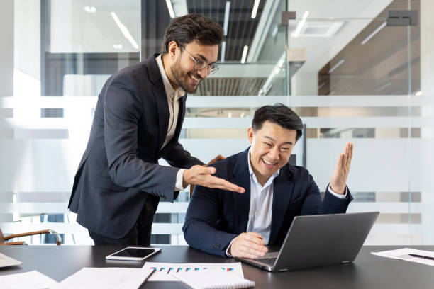 istock Two businessmen celebrating success while using a laptop in a modern office 2190104244