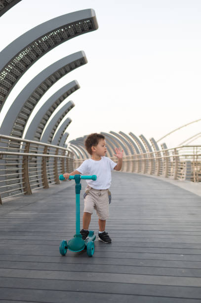 istock Multiracial Toddler Riding a Blue Three-Wheeled Scooter on a Modern Bridge 2190108119