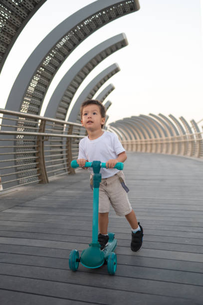 istock Multiracial Toddler Riding a Blue Three-Wheeled Scooter on a Modern Bridge 2190108161