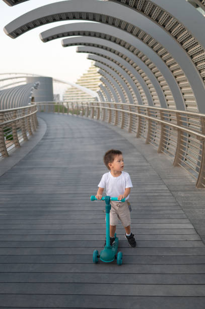istock Multiracial Toddler Riding a Blue Three-Wheeled Scooter on a Modern Bridge 2190108200