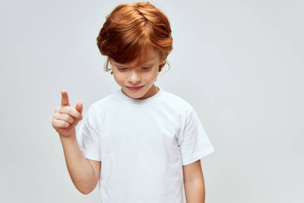 istock Red-haired boy looks down and shows his index finger up Copy space 2190110823