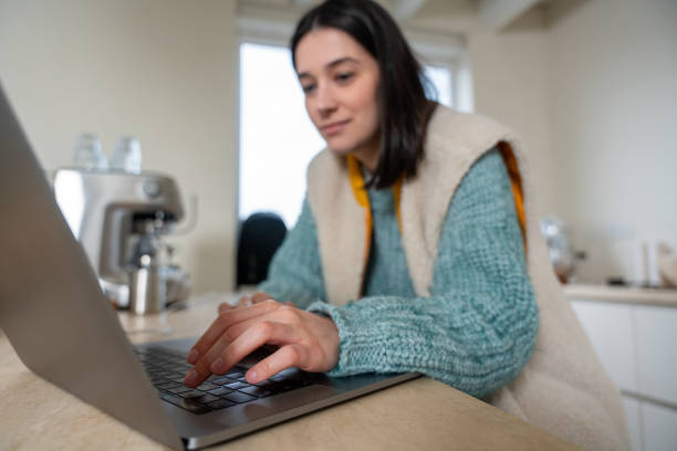 istock Young woman working from home on laptop in kitchen 2190114498