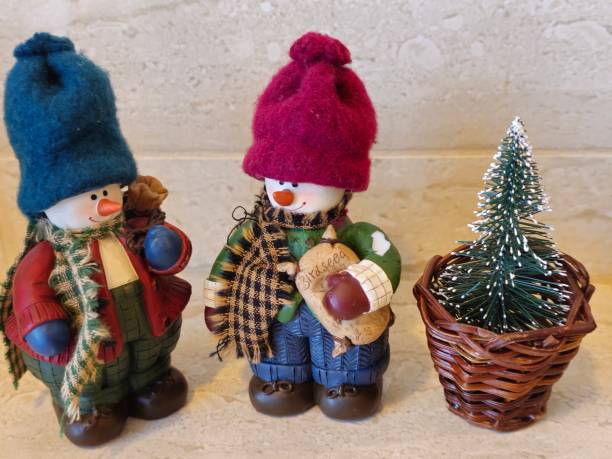 Two porcelain snowmen dressed up for winter, wearing hats, scarfs, winter boots and mittens. Each carrying a bag of bird seed to feed the birds.