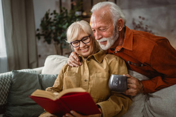 istock senior wife sit on sofa and read a book, while husband hug him 2190116524