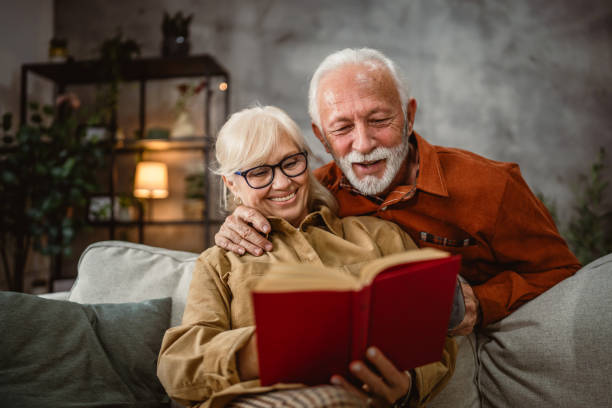 istock senior wife sit on sofa and read a book, while husband hug him 2190117065