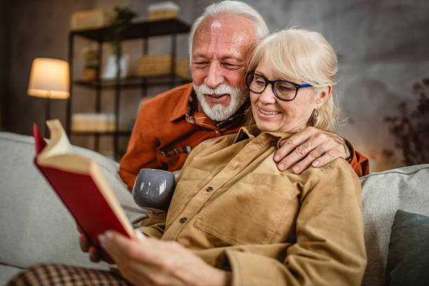 istock senior wife sit on sofa and read a book, while husband hug him 2190119058