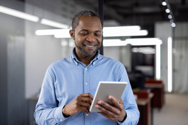 istock Mature African American businessman smiling while using tablet in modern office setting, showcasing technology in workplace and professional lifestyle 2190124821