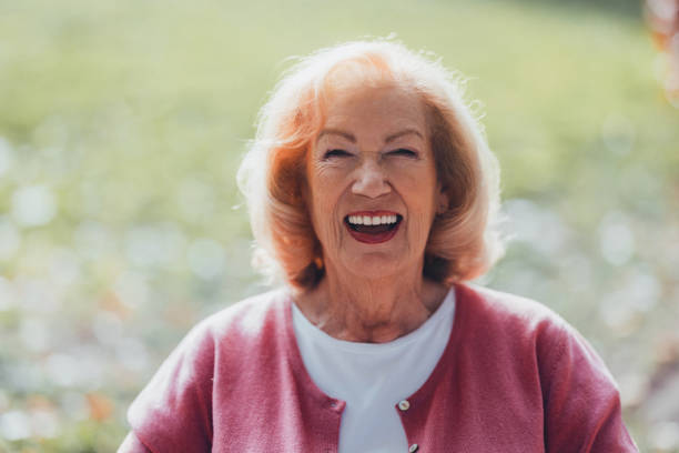 A cheerful elderly woman with a bright smile basking in sunshine amidst a natural green environment.