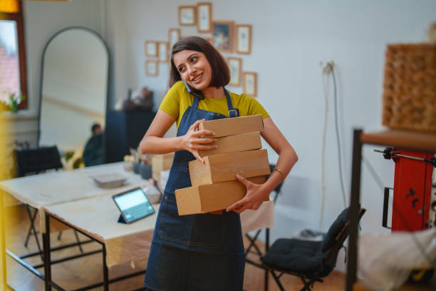 Young woman preparing shipping boxes is talking on the phone.