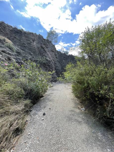 istock Narrow Gravel Pathway Winding Through Rocky Cliffs and Green Vegetation Under a Bright Blue Sky 2190130290