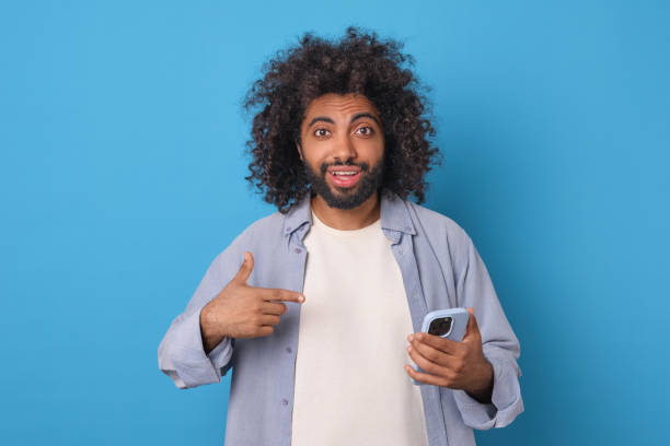 istock Engaging Young Man With Curly Hair Shows Smartphone in Vibrant Blue Setting 2190148680