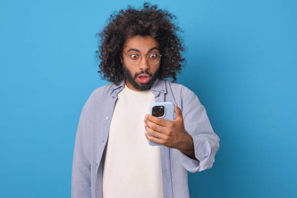 istock Surprised Man Checking His Phone Against a Vibrant Blue Backdrop 2190148685