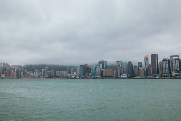 A stunning view of the Hong Kong skyline featuring towering skyscrapers and Victoria Harbour under heavy, overcast clouds.