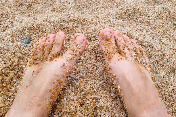 Bare feet partially submerged in coarse beach sand, evoking relaxation and summertime leisure. the warm tones of the sand complement the natural skin tones, creating a serene, carefree atmosphere ideal for travel and vacation themes.