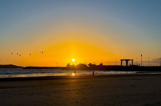 An emerging sun is rising over the calm waters of the Atlantic Ocean. Image is taken from Folly Beach County Park, outside of Charleston South Carolina.  The vivid orange sky is met be the dark blue water.