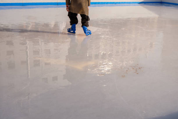 Smooth, shiny surface of an ice rink with reflected by spotlights. Dark empty ice arena with soft blue light. Concept of winter sports games, hockey, figure skating. Icy background of slippery ice, frosty space for training and performance.