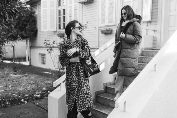 Black and white shot of two young fashionable female friends walking down the outdoor stairs while leaving house