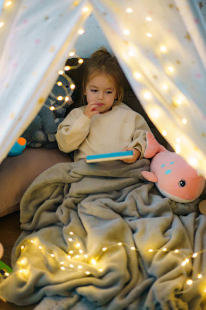 istock Girl holding a book while sitting in tent at home 2190178138