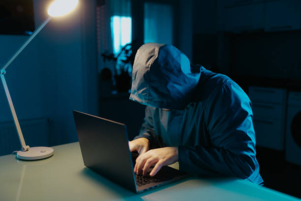 istock Cybersecurity Scene Hooded Man Focused on Laptop at Home Kitchen 2190180737