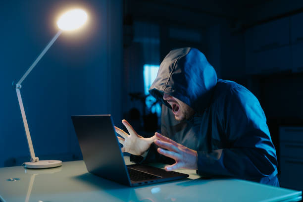 istock Frustrated hacker in hoodie slams hands in stress at dark table. 2190180756