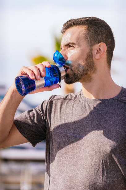 istock Athletic man drinking water from red bottle outdoors in city park.Vertical 2190181923