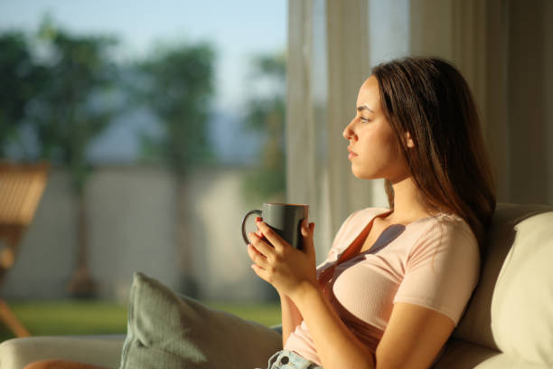 istock Serious woman thinking looking through a window drinking coffee 2190182910