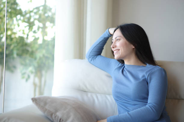 istock Happy asian woman relaxing looking through a window at home 2190183017