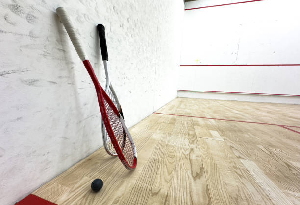 Two rackets and two squash balls lie on the parquet floor.