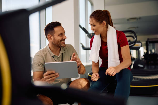 istock Happy fitness instructor and athletic woman analyzing exercise plans on digital tablet in a gym. 2190201678
