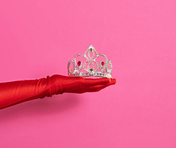 Women's hands in red gloves hold a crown on a pink background stock photo