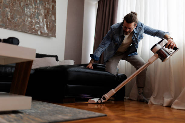 istock Man cleaning house with wireless vacuum cleaner 2190211815