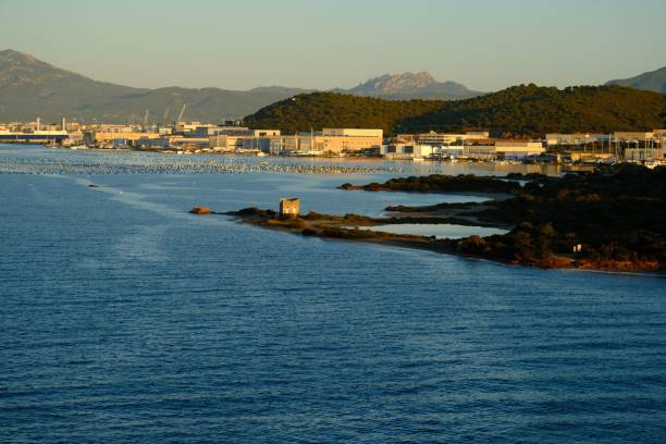 Scenic view of an industrial port and coastline with mountains in the backdrop during sunset.