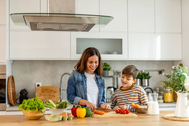 istock Mother and son smiling and having fun while preparing healthy meal with fresh vegetables in modern kitchen 2190212990