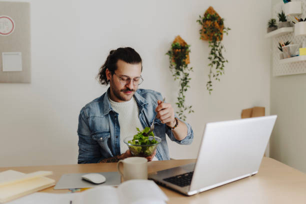 istock Man eating salad and using laptop 2190213118