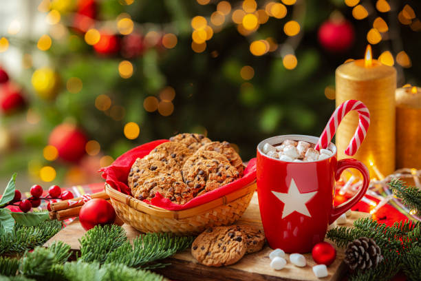 istock Hot chocolate marshmallow mug and chocolate chips cookies on Christmas decorated table near illuminated Christmas tree 2190215914