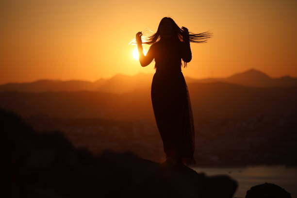 A joyful young Asian woman embraces the breathtaking beauty of a stunning sunset.
