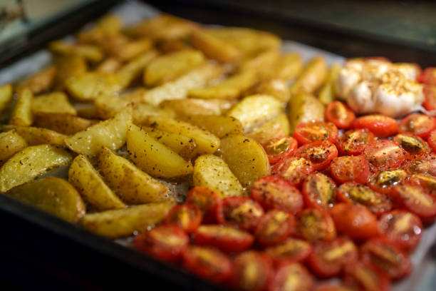 A close-up shot of roasted potatoes and tomatoes with garlic, freshly baked in the oven on a tray. The golden, seasoned potato wedges are paired with sweet, roasted cherry tomatoes, garnished with black pepper, and the garlic cloves, giving off a warm, savory aroma. Perfect for a healthy, easy-to-make side dish.
