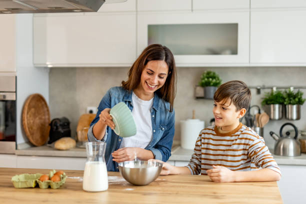 istock Mother and son happily baking together in their modern kitchen, pouring ingredients into a bowl 2190221002