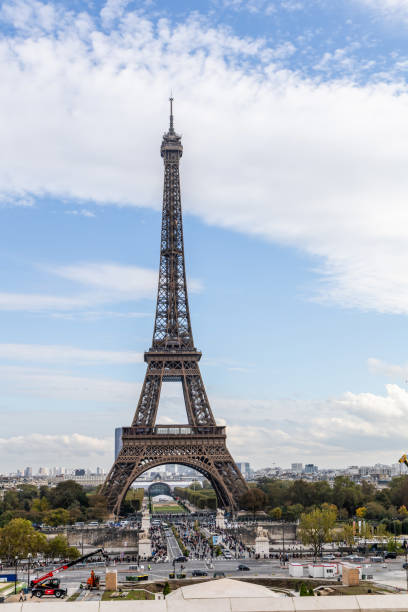 Eiffel Tower and street against cloudy blue sky with sun lensflare in Paris, France